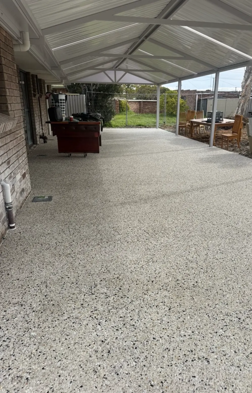 Exposed aggregate concrete floor under a patio roof, stones showing evenly across the slab