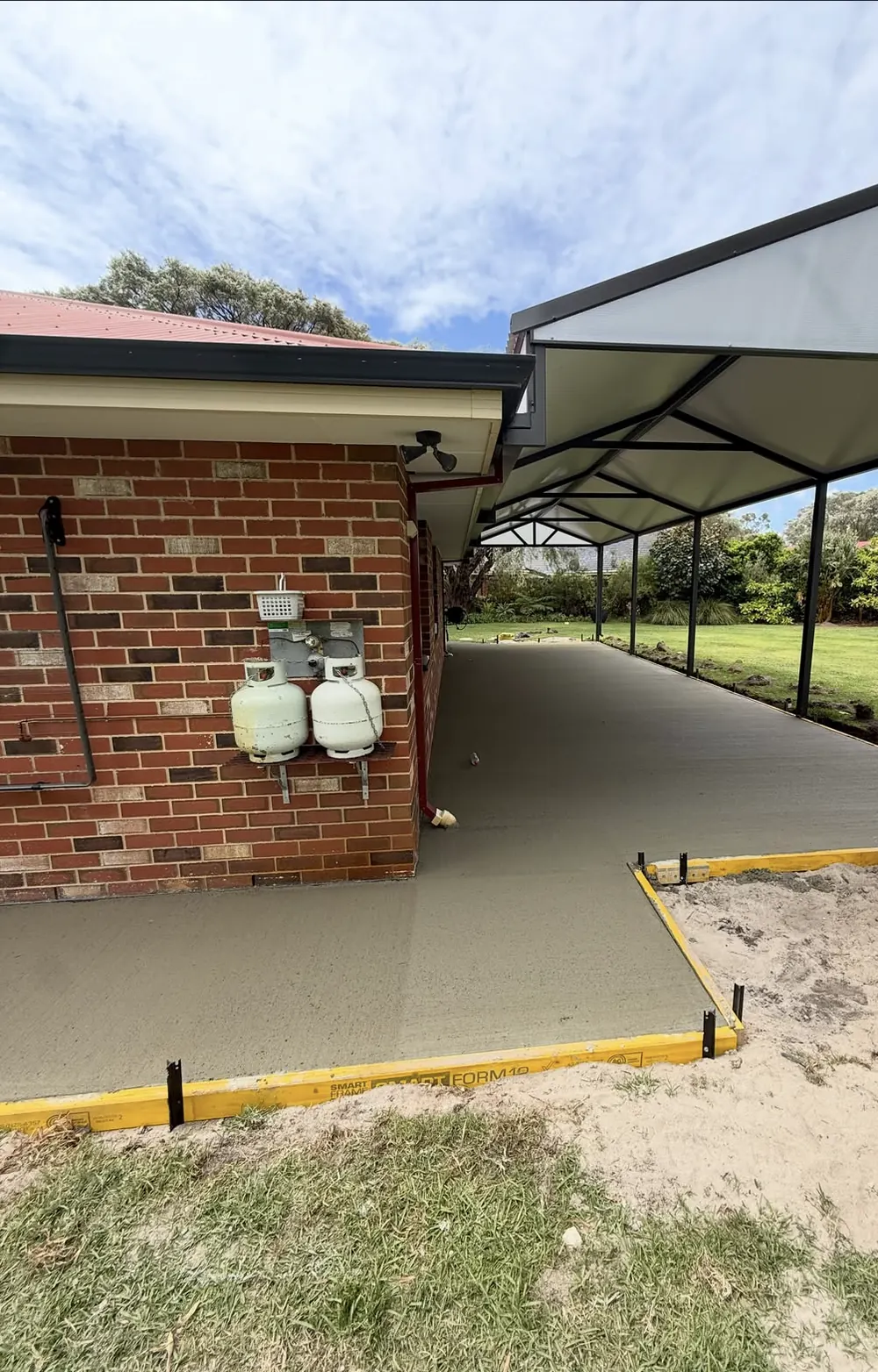Yellow formwork edging a freshly poured concrete path beside a brick house