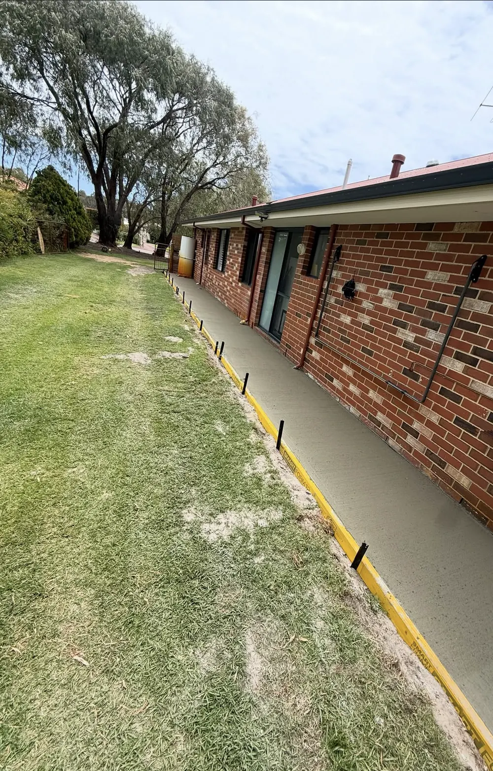 Broom-finished concrete path running along the side of a brick house