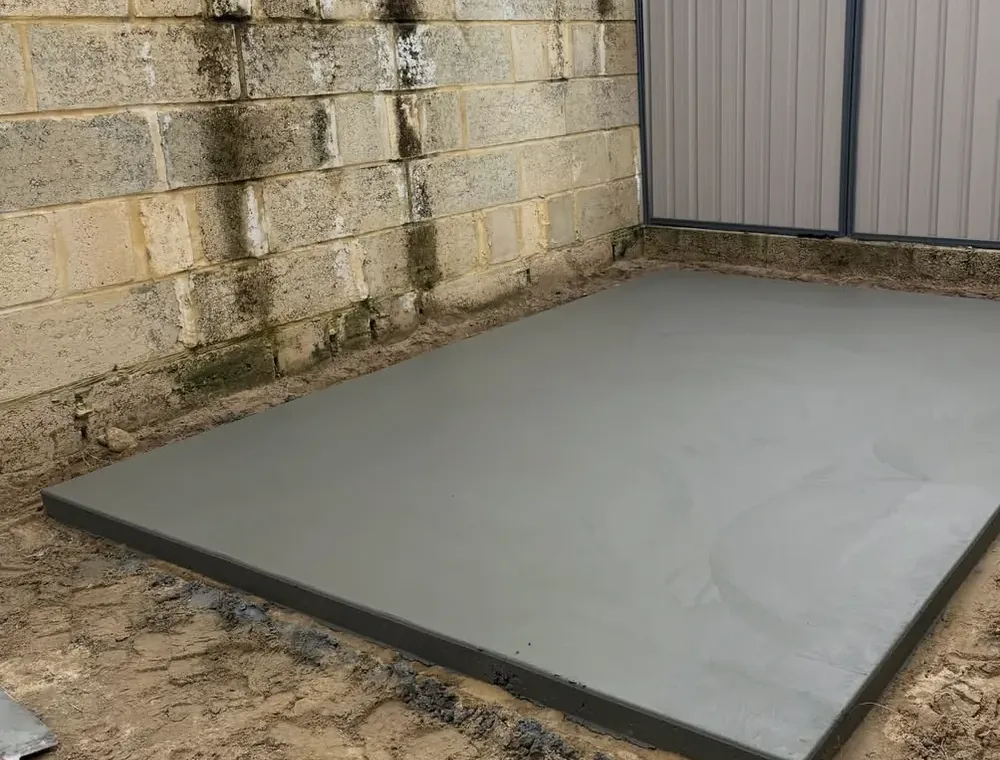 The finished shed pad slab against a limestone block wall and fence